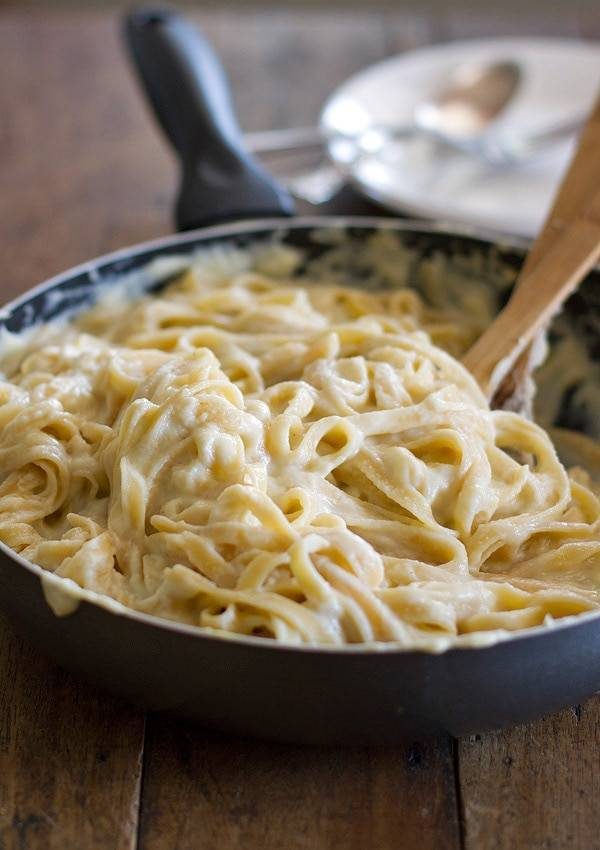 Fettuccine alfredo in a skillet with a wooden spoon.