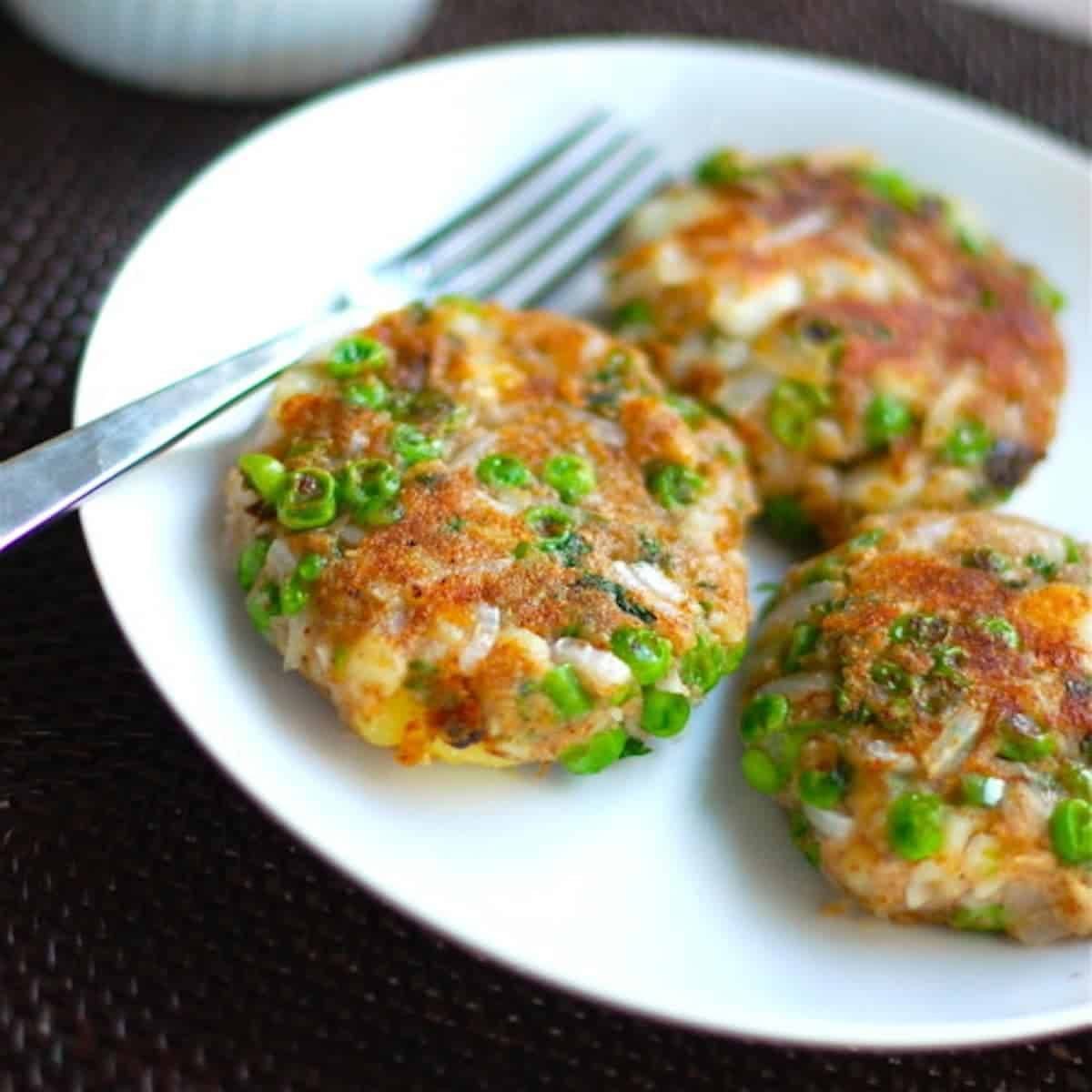 Aloo Tikki made with fried potatoes, peas, and onions on a white plate with a fork.