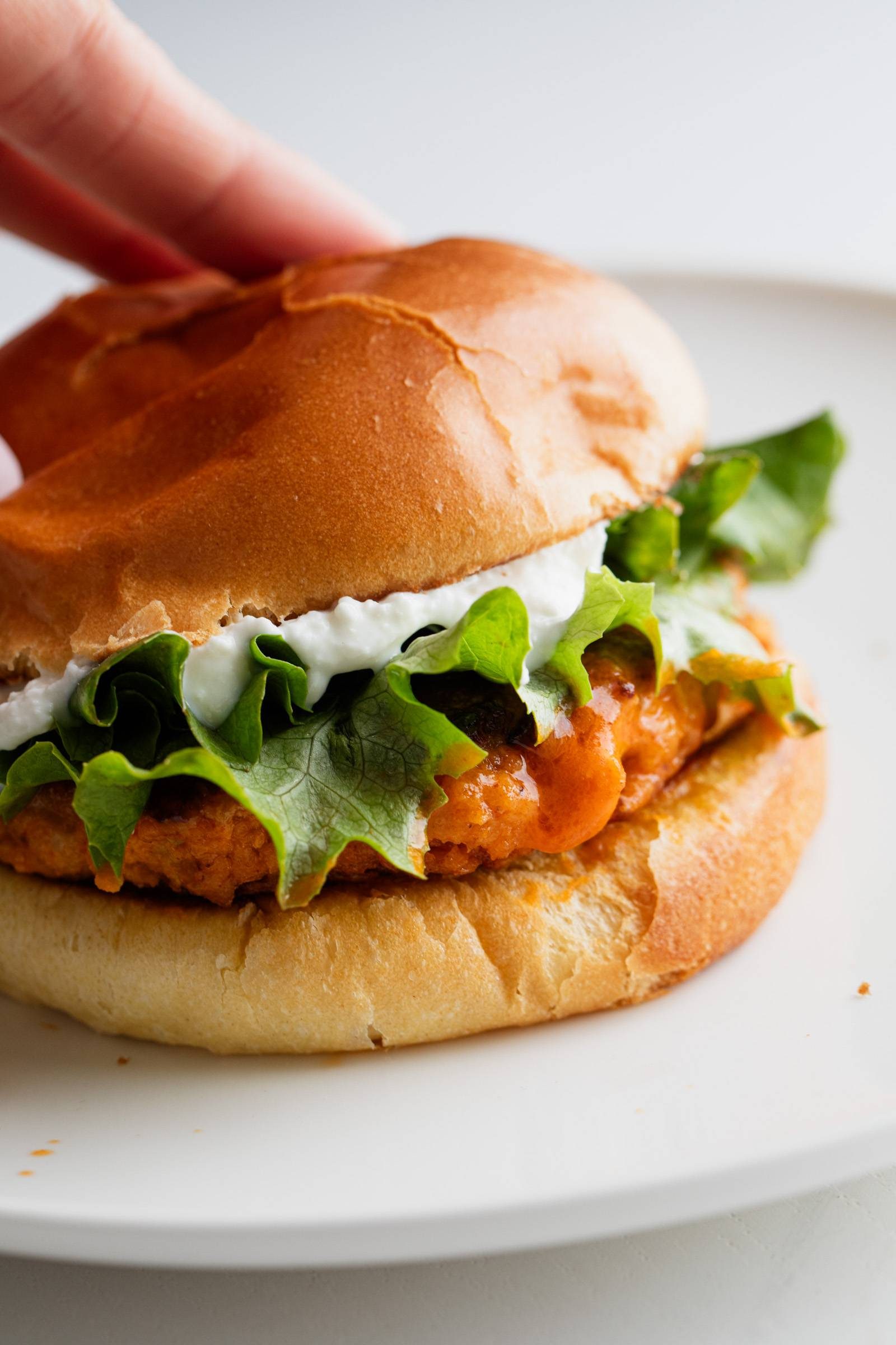 Buffalo chicken burger on a bun with lettuce and whipped feta spread.